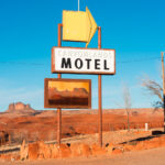 A photograph of a road sign for a motel with a yellow arrow in front of a bare desert landscape