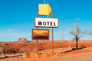 A photograph of a road sign for a motel with a yellow arrow in front of a bare desert landscape